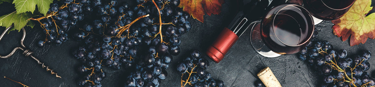 Rotwein, Korkenzieher und Glas mit Weintrauben und Herbstblättern auf einer dunkel strukturierten Oberfläche.