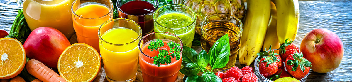 Orangensaft neben Saftgläsern und verschiedenen Früchten