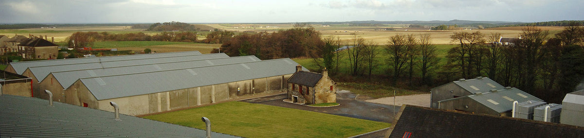 Blick auf die Ballantine’s Whisky Destillerie in Schottland, umgeben von Feldern und traditioneller Architektur