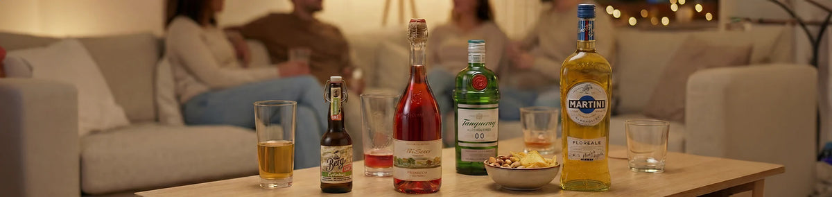 Flaschen mit Alkohol, Snacks und Gläsern auf einem Tisch mit vier Personen, die auf einem Sofa im Hintergrund sitzen.