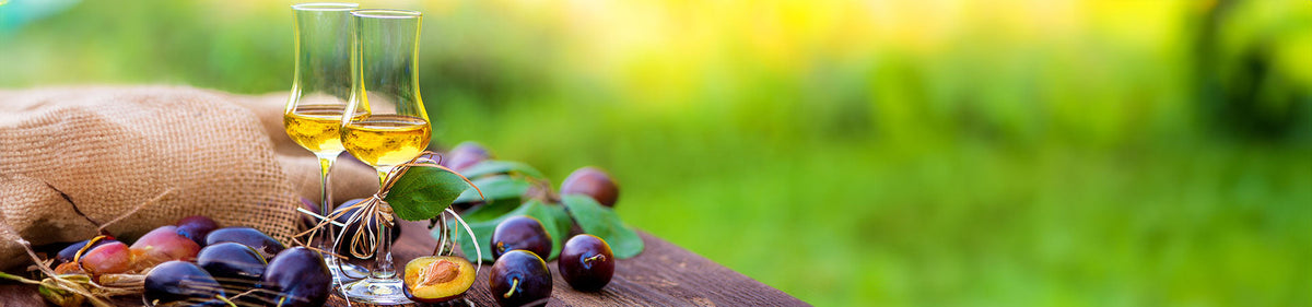 Verschiedene Obstbrände in Grappagläsern auf einem Holztisch neben Früchten