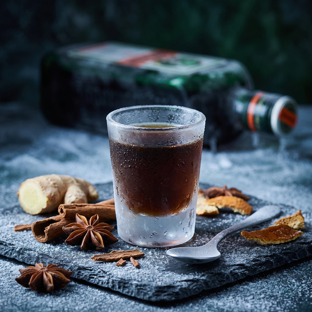 Jägermeister Glas umgeben von Kräutern und einer Flasche im Hintergrund