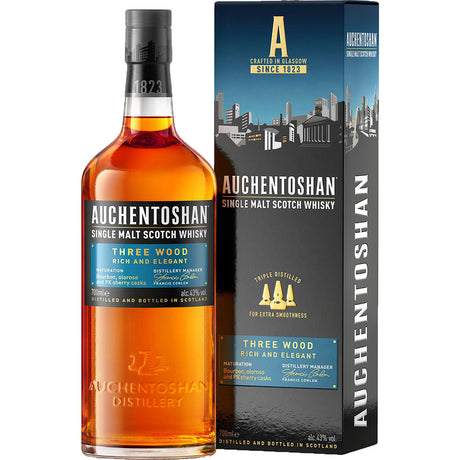 Eine Flasche Auchentoshan Three Wood Single Malt Scotch Whisky 43% 0.7L ist neben der Markenschachtel abgebildet, die beide das Logo von Auchentoshan und die Produktangaben enthalten.