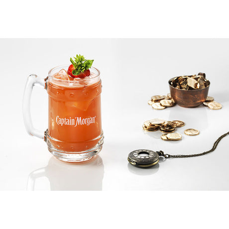Ein Captain Morgan Becher mit einem Orangencocktail, Eis und Garnitur steht neben Goldmünzen und einer Kompasskette und fängt die abenteuerliche Essenz von Captain Morgan Spiced Gold 35% 0,7 Liter ein.
