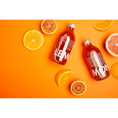 Zwei Flaschen Lemonaid Blutorange 0,33L auf einem orangefarbenen Hintergrund mit Zitrusscheiben, von oben betrachtet - ein lebhaftes Schaufenster für die fair gehandelten Bio-Getränke von Lemonaid.