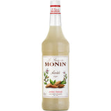 Eine 1-Liter-Flasche Monin Mandel Sirup von Monin mit einem weißen Etikett, auf dem Mandeln und Mandelblüten abgebildet sind.