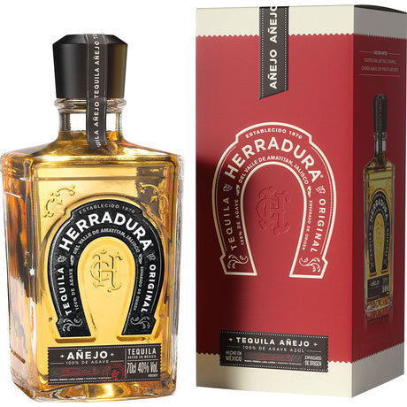 Eine Flasche Herradura Tequila Anejo 40% 0,7 Liter steht neben der rot-weißen Schachtel - ein Premium-Tequila aus 100% blauer Weber-Agave, perfekt für jede Gelegenheit.